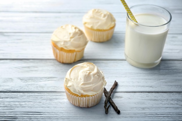 Sabrosos cupcakes de vainilla y un vaso de leche sobre una mesa de madera