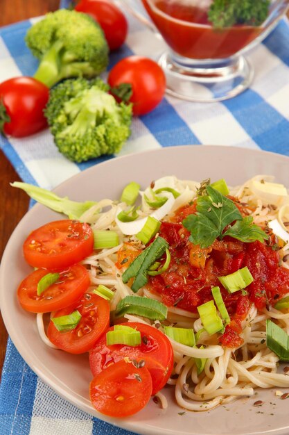 Foto sabrosos espaguetis con salsa y verduras en un plato sobre una mesa de madera cerrada