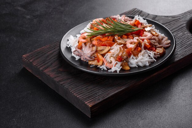 Sabrosos fideos de arroz con tomate, pimiento rojo, champiñones y mariscos sobre un fondo de hormigón oscuro