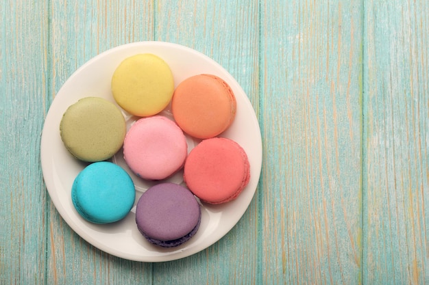 Sabrosos macarrones de colores en un plato pequeño sobre fondo de madera de color