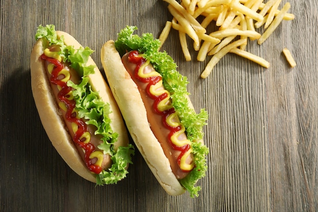 Sabrosos perritos calientes con papas fritas sobre fondo de madera