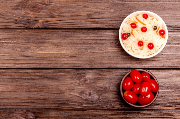 Sabrosos productos caseros de leche fermentada en platos - chucrut, tomates en escabeche, en mesa de madera, espacio de copia.