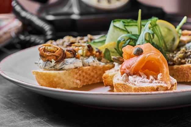 Sabrosos sándwiches italianos con mariscos contra el fondo de madera rústica. Crostini con queso, pescado rojo, limón y aceitunas en rodajas, vista horizontal con enfoque selectivo