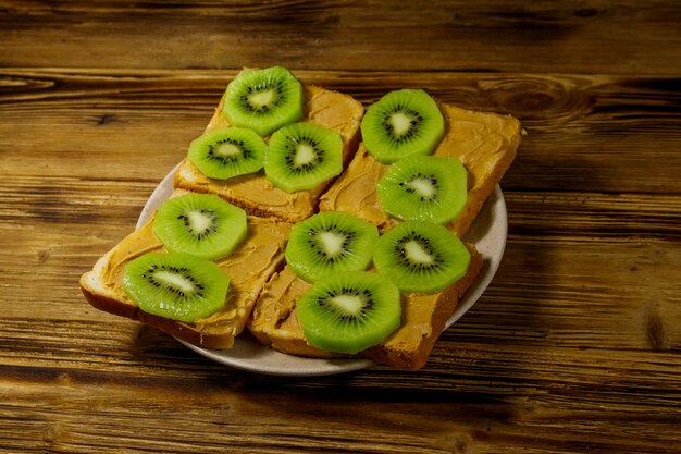 Sabrosos sándwiches con mantequilla de maní y kiwis en mesa de madera