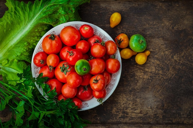 Sabrosos tomates rojos, amarillos y verdes con verdor verde en el plato