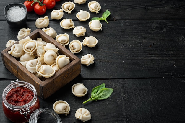 Sabrosos tortellini crudos con harina y albahaca, sobre fondo de mesa de madera negra, con copyspace y espacio para texto