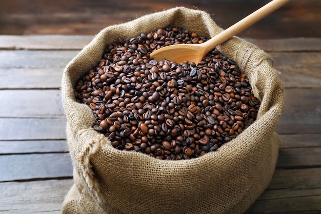 Sac con granos de café tostados con cuchara sobre mesa de madera