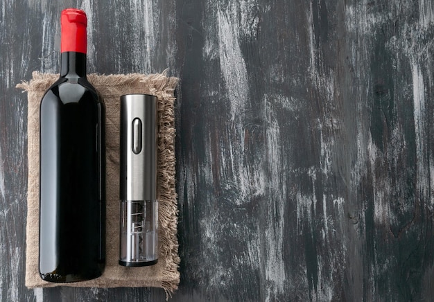 Foto sacacorchos eléctrico gris hecho de metal se encuentra junto a una botella de vino sobre tela de lino fondo de madera oscura vista desde arriba