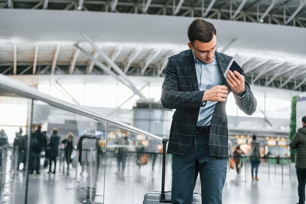 Sacando los documentos El joven hombre de negocios con ropa formal está en el aeropuerto durante el día