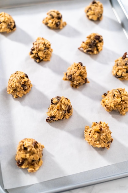 Sacar la masa para galletas con una cuchara de masa en una bandeja para hornear forrada con papel pergamino para hornear galletas suaves de avena, pasas y nueces