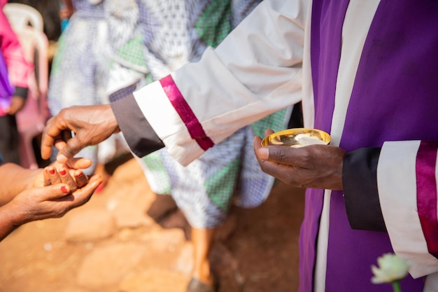 Un sacerdote africano le da pan sacramental a un creyente centrado en la mano con pan sacramental