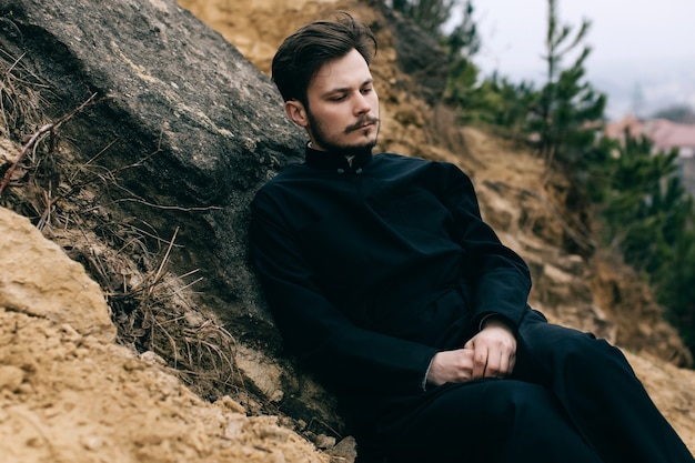 Sacerdote católico barbudo posando al aire libre en las montañas