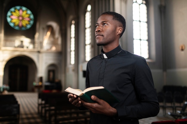 Foto sacerdote masculino joven que sostiene el libro sagrado en la iglesia