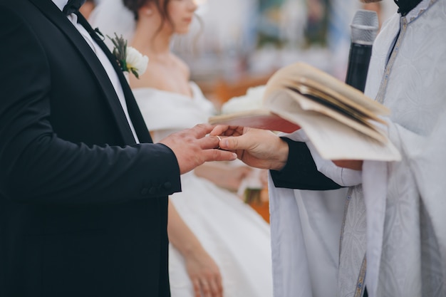 Foto sacerdote pone anillo en el dedo del novio durante la ceremonia de boda ortodoxa