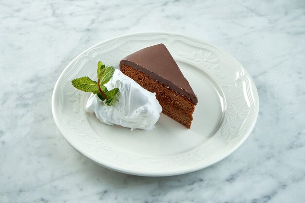 Sachertorte vienés clásico servido en un plato blanco sobre una mesa de mármol. Pastel de chocolate sacher austriaco