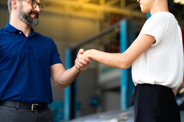 Sachkundiger Mechaniker, der zufriedenen Kunden die Hände schüttelt und in der Garage der Autoreparaturwerkstatt arbeitet. Zufriedenheit im Service.