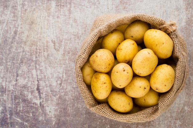 Sack frische rohe Kartoffeln auf hölzernem Hintergrund, Draufsicht.