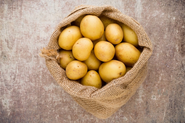 Sack frische rohe Kartoffeln auf hölzernem Hintergrund