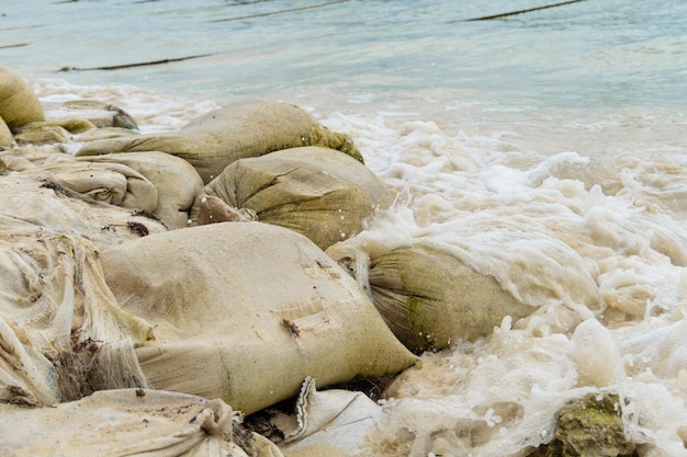 Saco de areia para enchente na beira do mar As ondas batem nos sacos de areia o mar está inquieto