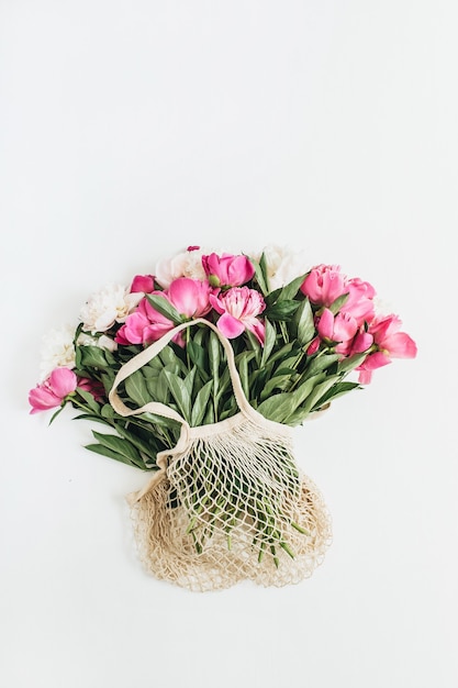 Saco de barbante com flores de peônia rosa e branca na superfície branca