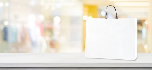 Saco de compras de papel branco em pé na mesa de mármore branca