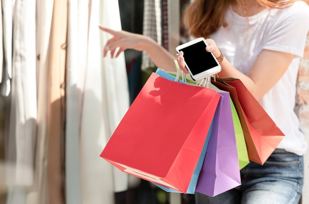 Saco de compras levando da menina de compra com smartphone à disposição.