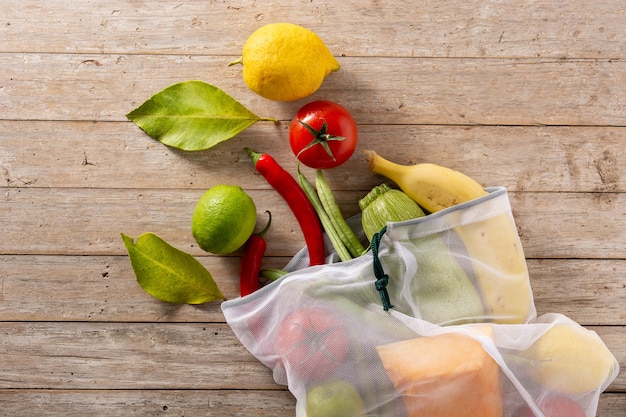 Saco de compras reutilizável ecológico com legumes e frutas na mesa de madeira