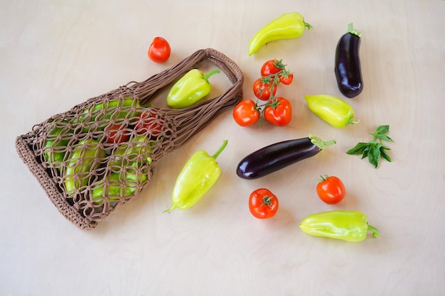 Saco de corda marrom tricotado na técnica de macramê a partir de um cordão de malha com pimentão verde e tomate em um fundo de madeira Vista superior plana leiga Zero desperdício e conceito livre de plástico