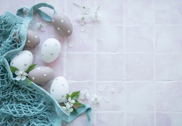 Saco de cordas com ovos de páscoa e flor de primavera em fundo de azulejo rosa