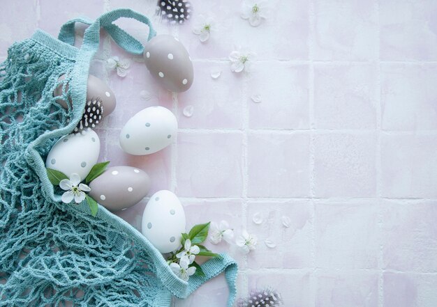 Saco de cordas com ovos de páscoa e flor de primavera em fundo de azulejo rosa