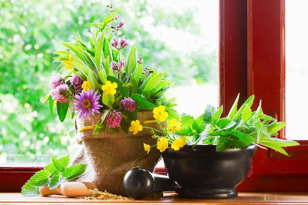 Saco de ervas medicinais curativas e argamassa de flores e pilão no peitoril da janela Medicina alternativa