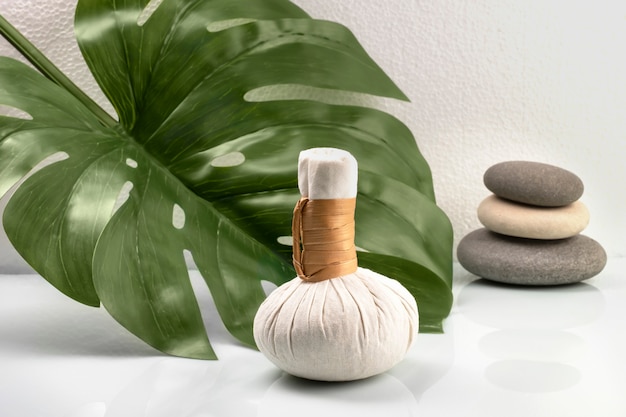 Saco de kit de massagem com ervas e pedras no fundo com folhas de monstera