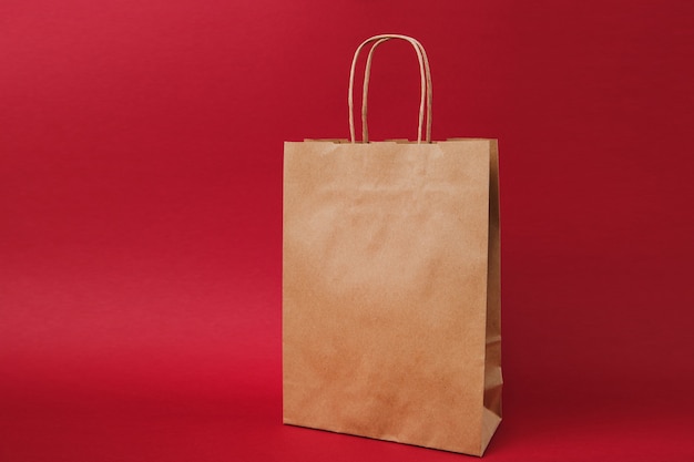 Saco de pacote, saco de papel artesanal em branco claro marrom para take-away isolado em fundo vermelho brilhante. Serviço de entrega de produtos alimentícios da loja ou restaurante para o escritório de trabalho. Simule o espaço da cópia.