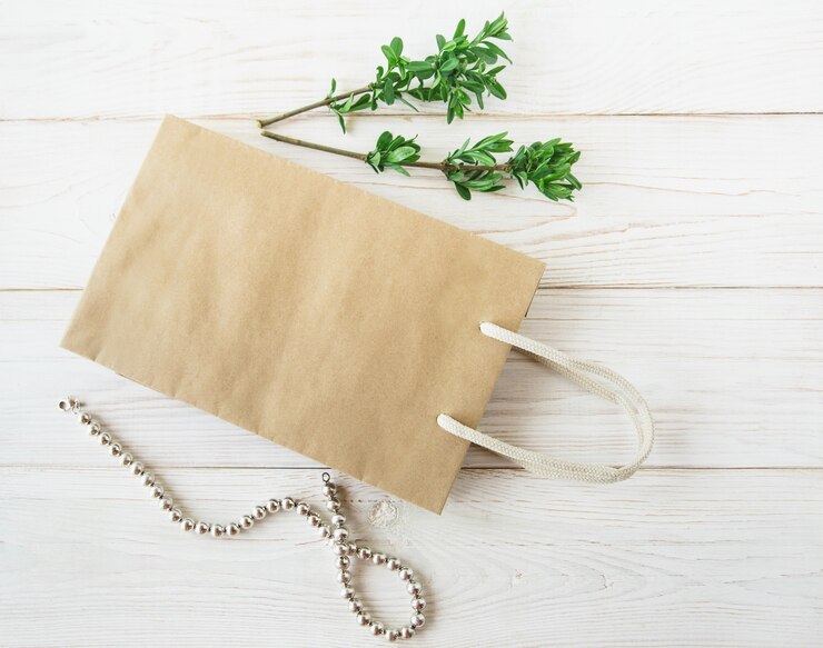 Saco de papel artesanal em branco com alças, folhas verdes frescas e colar. Fundo branco