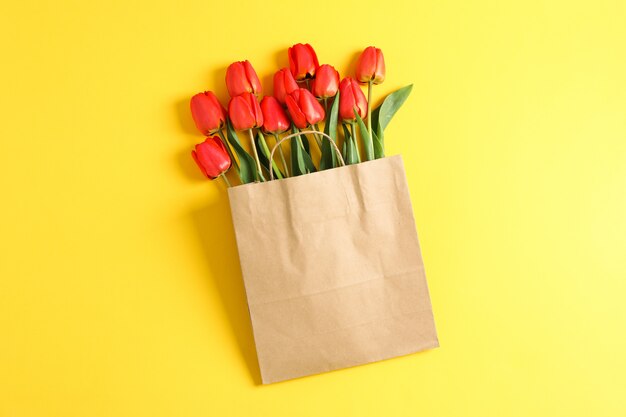 Saco de papel com lindas tulipas vermelhas em fundo amarelo, espaço para texto