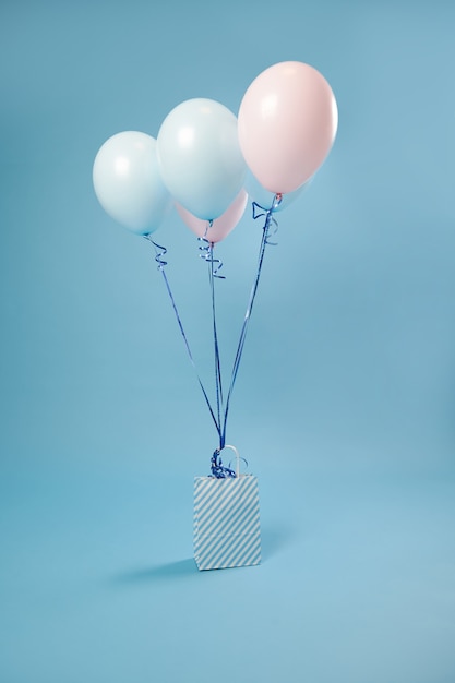 Saco de papel com listras branco-azul e balões coloridos rosa-azul