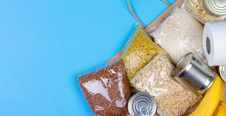 Foto saco de papel com um suprimento alimentar de crise pelo período de isolamento em quarentena do coronavírus, arroz, macarrão, aveia, comida enlatada, papel higiênico, trigo sarraceno, banana em um fundo azul