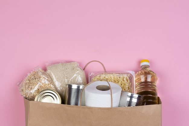 Saco de papel com um suprimento de comida de crise pelo período de isolamento de quarentena em um fundo rosa