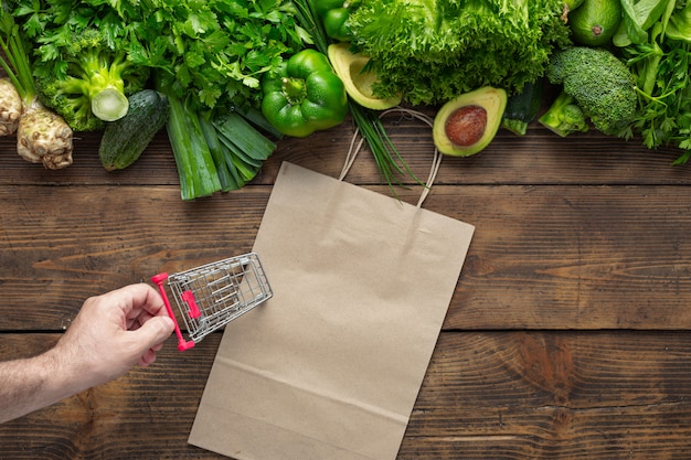 Saco de papel com vegetais verdes e pequeno carrinho de compras. compre comida vegetariana e vegetariana saudável