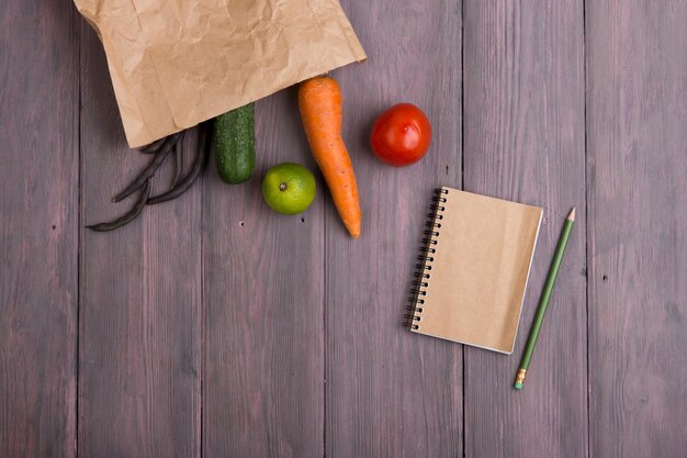 Saco ecológico de papel de conceito de comida vegetariana saudável com vários vegetais saudáveis e bloco de notas em branco para receita