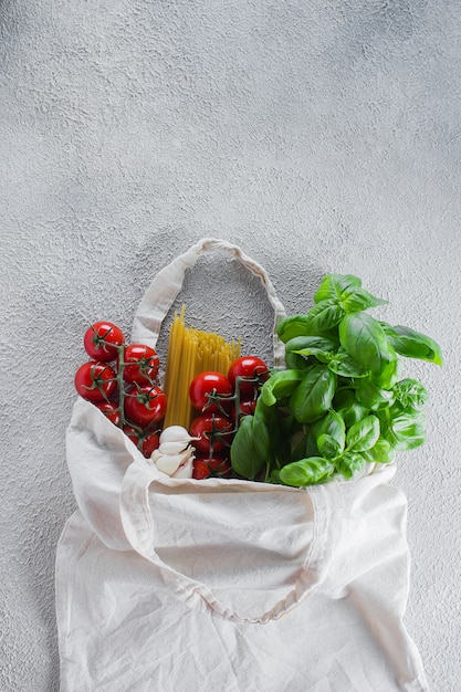 Saco reutilizável com mantimentos. sacola, desperdício mínimo. manjericão, tomate cereja, alho em saco de tecido