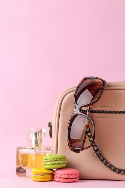 Saco rosa na moda elegante e macaroons franceses e bolos de perfume, óculos em um fundo rosa na moda brilhante. conceito de acessório feminino.