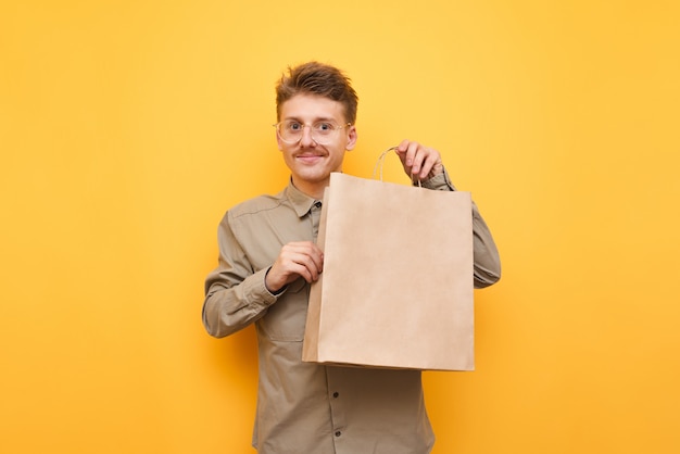 Sacola de compras em saco de papel isolado em amarelo, olhando na câmera e sorrindo