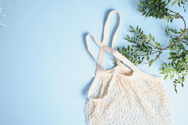 Sacolas de compras de malha reutilizável e folhas verdes sobre fundo azul. conceito de desperdício zero.