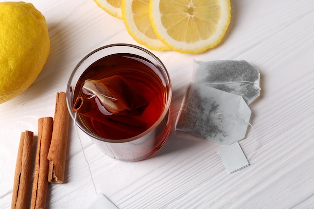 Sacos de chá copo de paus de canela de bebida quente e limões na mesa de madeira branca acima da vista