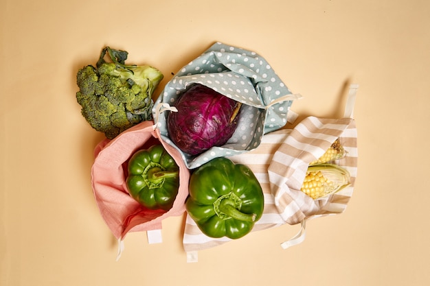 Sacos de compras de algodão de pano para mantimentos com legumes. Fundo bege. Sem plástico