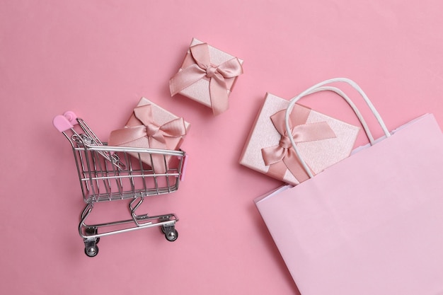 Sacos de compras de papel com caixas de presente e carrinho de compras em fundo rosa pastel Vista superior