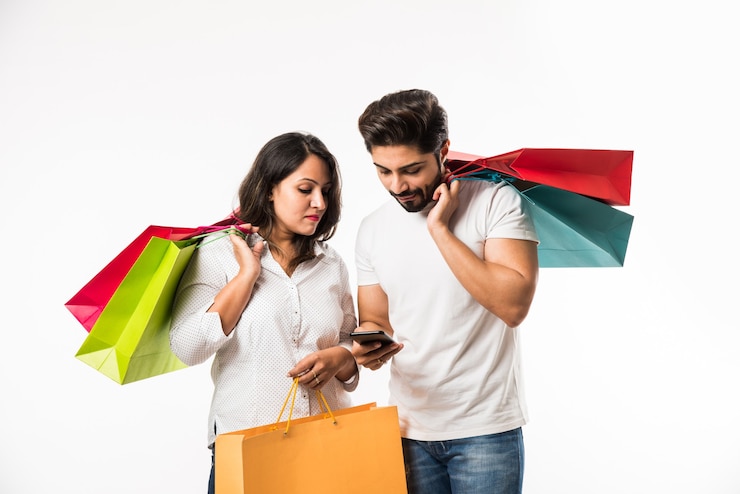 Foto sacos de compras do jovem casal indiano e telefone inteligente ou celular, clicando em selfie ou localizando loja, isolado sobre fundo branco. foco seletivo