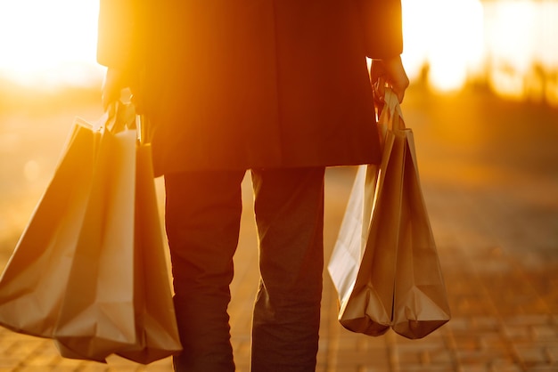 Sacos de compras nas mãos ao pôr do sol Mão de jovem com sacos de papel com compras