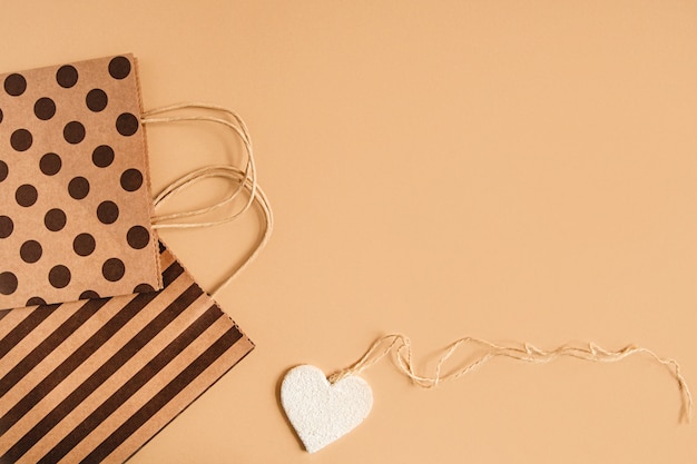 Sacos de embalagem com alças de bolinhas e listras e uma figura em forma de coração em um fundo de artesanato. postura plana com copyspace